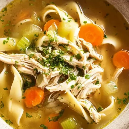 A steaming bowl of homemade chicken noodle soup with fresh herbs.