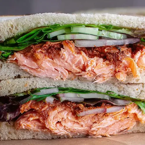 A freshly prepared salmon sandwich on whole wheat bread with greens.